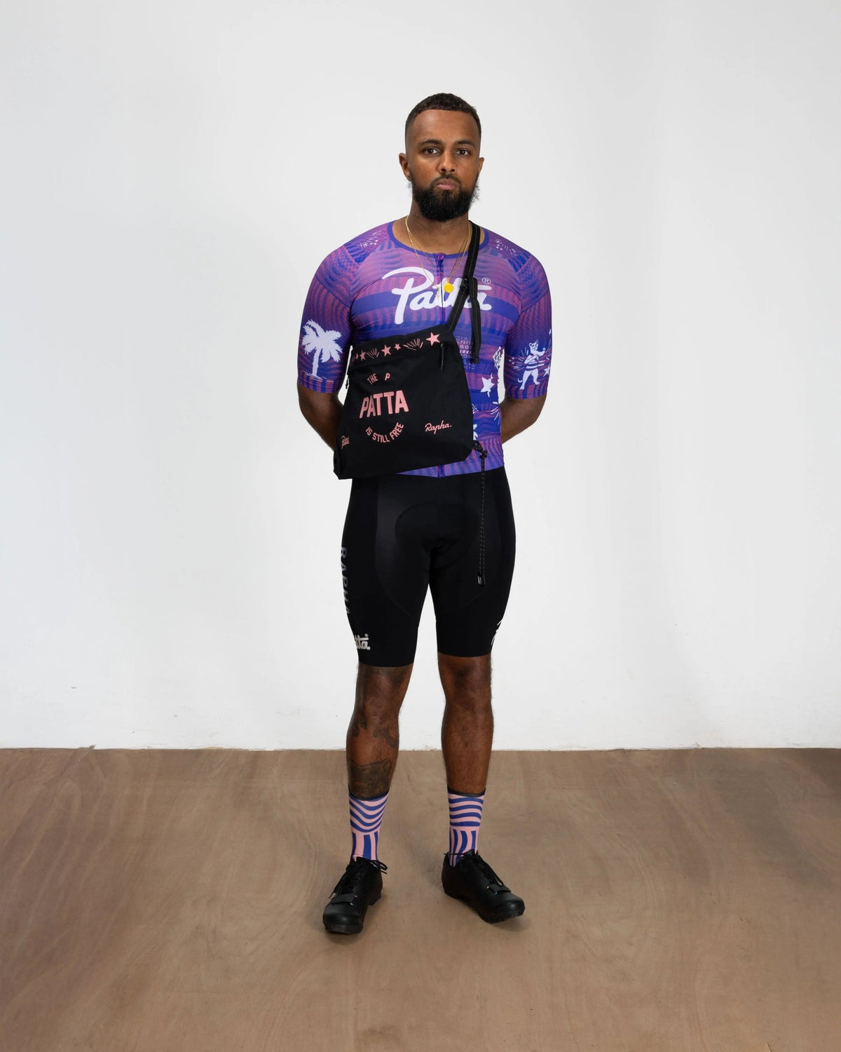 Model wearing the black and pink Patta x Rapha Tech Musette crossbody bag in full cycling kit.