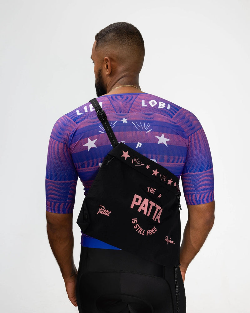 Patta x Rapha Tech Musette in black and pink worn across the back over a cycling jersey.