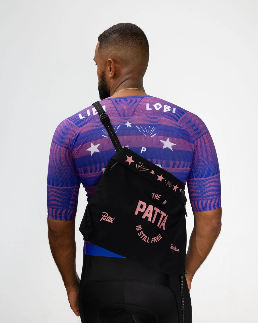Patta x Rapha Tech Musette in black and pink worn across the back over a cycling jersey.