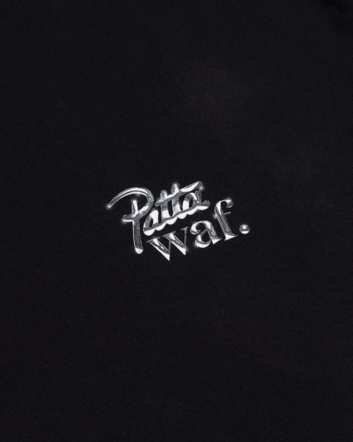 Close-up of the metallic silver Patta x waf. chest logo on a black cotton kids t-shirt.
