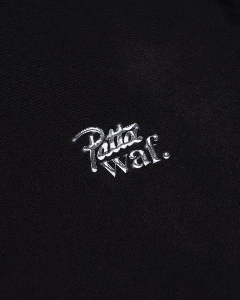 Close-up of the metallic silver Patta x waf. chest logo on a black cotton kids t-shirt.