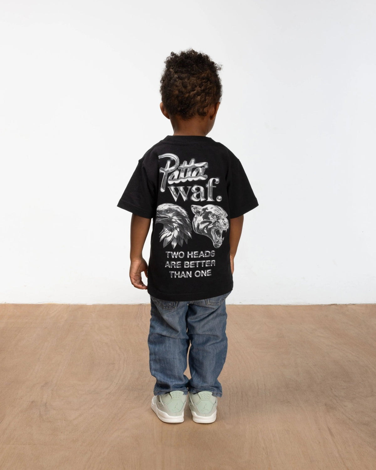 Back view of a child wearing the black Patta x waf. Homecoming 2025 graphic t-shirt.